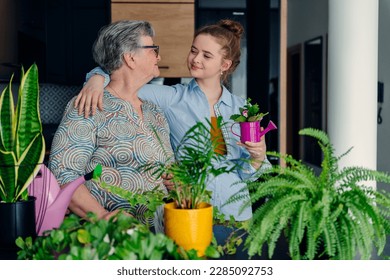 Two happy different generetion females enjoy, embracing, spending time together. Elderly grandmother teaches sharing experience cute teenage girl caring for a houseplant at home in the kitchen. - Powered by Shutterstock