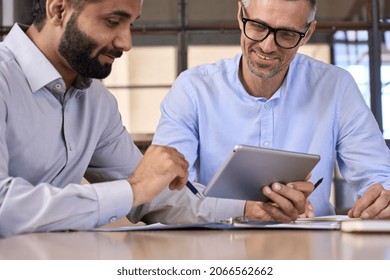 Two happy diverse business men discussing analyzing financial market data using digital tablet. Financial advisor broker manager consulting investor client managing project tech at office meeting.