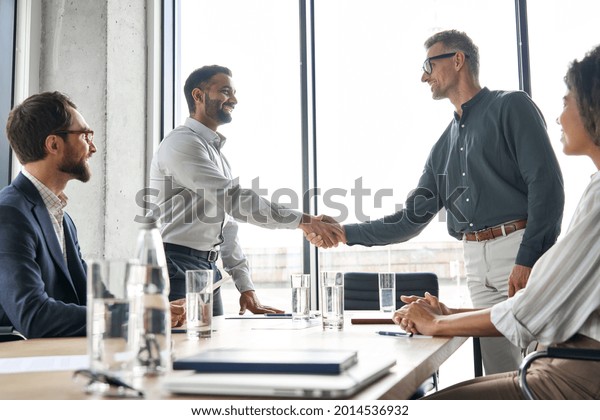 Two happy diverse professional business men\
executive leaders shaking hands after successful financial deal at\
group board office meeting. Trust agreement company trade\
partnership handshake\
concept.