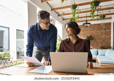 Two happy executive managers working on laptop discussing financial documents at meeting. Smiling friendly man and woman business professionals team talking planning project at work. Candid photo. - Powered by Shutterstock