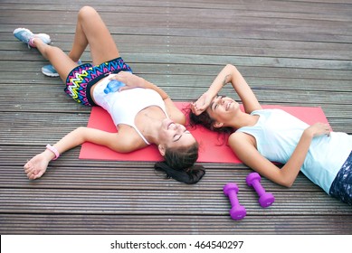 Two happy fit young women friends lying down tired after workout exercising in a park. Active healthy lifestyle concept - Powered by Shutterstock