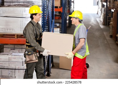 Two happy foremen carrying cardboard box at warehouse