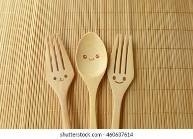 Two happy forks with one happy spoon on wood texture of dining table. Concept about happiness and friendship.