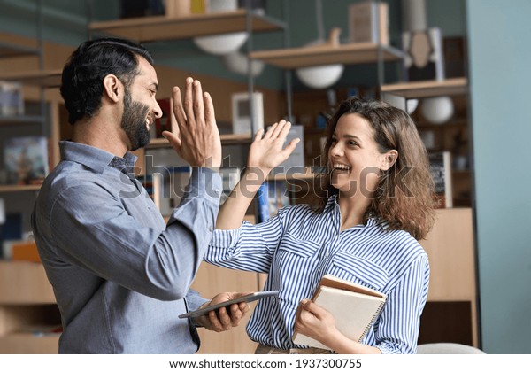 Two happy friendly diverse professionals, teacher\
and student giving high five standing in office celebrating\
success, good cooperation result, partnership teamwork and team\
motivation in office work.