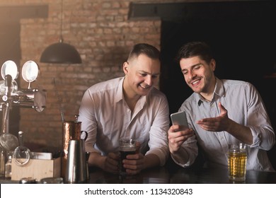 Two happy friends enjoying fresh beer at pub and browsing social networks on mobile. Technologies, online communication and internet addiction, copy space - Powered by Shutterstock