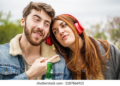 Two Happy Friends Sharing Headphones Listening To Their Favorite Song Sitting Together In The Parkland - People And Technology Concept