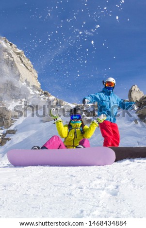 Two happy friends snowboarders are having fun on ski slope with snowboards in sunny day and cliff background.
