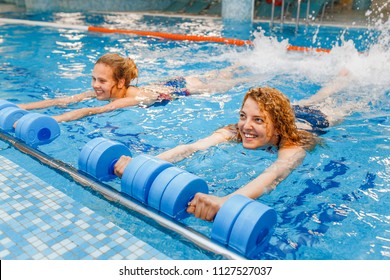 Two happy girls exercising in swimming pool with dumbbells. aqua aerobics classes concept