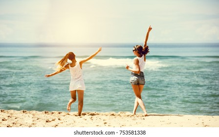 Two Happy Girls Friends Are Having Fun At Sea Beach. Jumping And Dancing