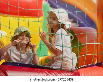 Two Happy Girls Play In Bounce House.Kids Plays In Bouncing Inflatable Castle Outdoor.Happy Small Girls,children Playing In Bouncy Castle Playground Outside In Summer Day