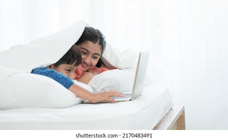 Two happy Indian brother and sister in traditional clothing lying on bed under blanket smiling, using laptop, having fun together at home. Education, Siblings relationship concept. Selective focus - Powered by Shutterstock