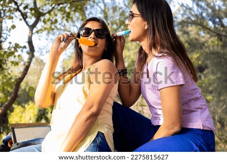 Two Happy indian women enjoying ice lolly or ice candy in hot summer day. Heat stroke.