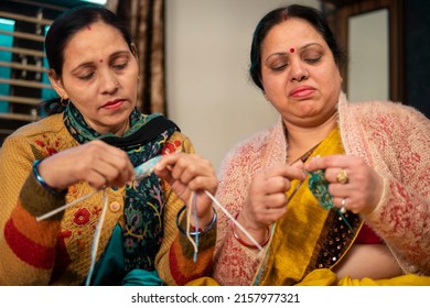 Two Happy Indian Women Sitting Together And Knitting A Warm Sweater With Woolen Thread At Home In Winter.