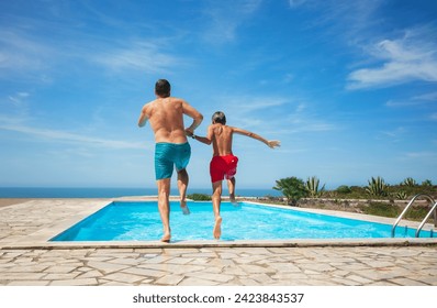 Two happy individuals, dad and teen son are enjoying a sunny day by jumping into a clear outdoor swimming pool overlooking the ocean - Powered by Shutterstock