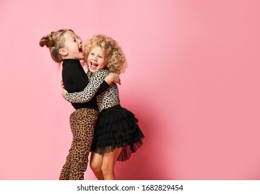 Two Happy Kids Blonde Girls Best Friends Sisters In Leopard Print Clothes Pants And Sweater Are Hugging Laughing Over Pink Background With Free Copy Space