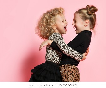 Two Happy Kids Girls Best Friends Sisters In Leopard Print Clothes Pants And Sweater Are Hugging Looking At Each Other Laughing Having Fun On Pink Background