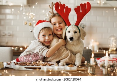 Two happy kids hugging embracing with golden retriever puppy while making xmas cookies at home during winter holidays, cute little children behind kitchen table having fun with dog at Christmas time