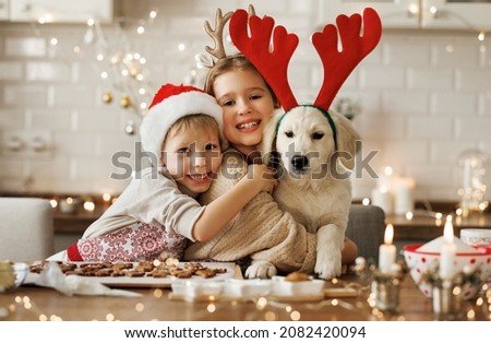 Two happy kids hugging embracing with golden retriever puppy while making xmas cookies at home during winter holidays, cute little children behind kitchen table having fun with dog at Christmas time