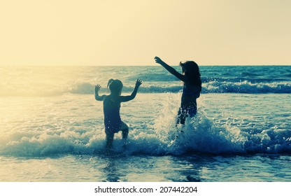 Two Happy Kids Playing On The Beach At Sunset