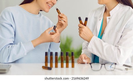 Two Happy Ladies Who Own Small Perfumery Business Sitting At Lab Table With Little Brown Glass Rollerball Bottles And Smelling Various Essential Oils Or Different Perfume Samples. Aromatherapy Concept