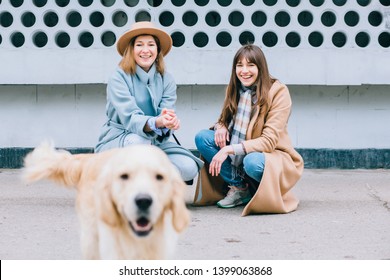 Two Happy Laughing Adult Twins Female Sisters With Running Away Dog. Training Golden Retriever, The Performance Of The Teams.