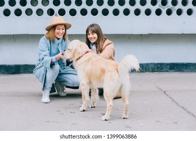 Two Happy Laughing Adult Twins Female Sisters With Running Away Dog. Training Golden Retriever, The Performance Of The Teams.