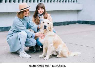 Two Happy Laughing Adult Twins Female Sisters With Running Away Dog. Training Golden Retriever, The Performance Of The Teams.