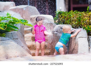 Two happy laughing children, adorable toddler girl and little baby boy, brother and sister, playing together with water tap in a pool on a hot summer day