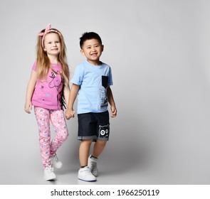 Two happy laughing, smiling kids friends Asian boy and Caucasian girl in summer clothes have good time together, walking coming to us holding hands over light background with copy space - Powered by Shutterstock