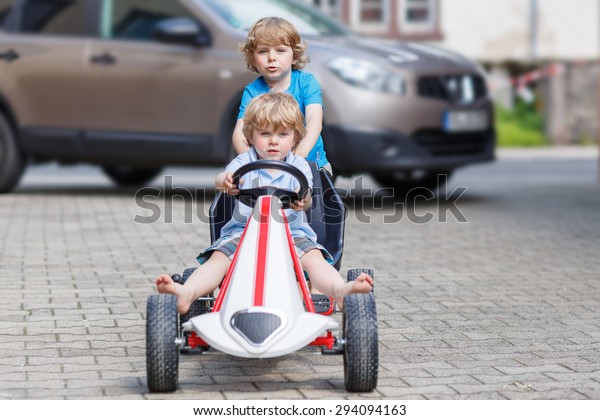 Two happy
little boy friends having fun with toy race car in summer garden,
outdoors. Active kid pushing the car with younger boy. Outdoor
games for children in summer
concept.