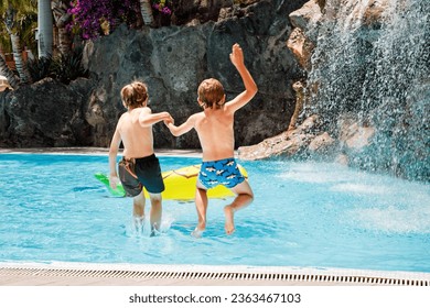 Two happy little kids boys jumping in the pool and having fun on family vacations in a hotel resort. Healthy children, siblings and best friends playing in water