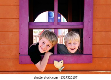 Two Happy Little Kids, Brothers, Are Smiling At The Park As They Peek Out The Window Of A Clubhouse Fort.