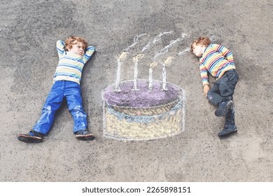 Two happy little kids having fun and big birthday cake picture drawing and colorful chalks  Creative leisure for children outdoors in summer  Kids blowing candles