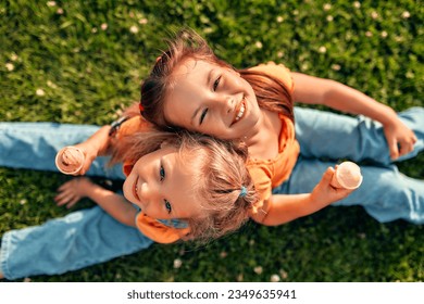 Two happy little sister girls sitting in a meadow on the grass in the park and eating ice cream, playing and having fun together on a warm sunny weekend. - Powered by Shutterstock