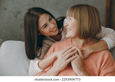 Two happy lovely adult women mature mom young kid wear casual clothes hug look to each other sit on gray sofa couch stay at home flat rest relax spend free spare time in living room. Family concept - Powered by Shutterstock