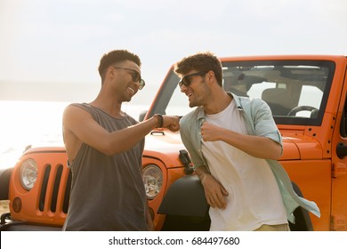 Two Happy Male Friends Having A Good Time Together At The Beach With A Car On Background