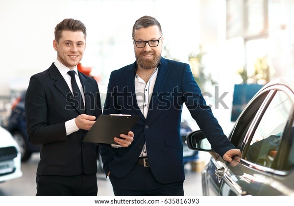 Two\
happy men in car dealership. Salesmen and\
buyer.