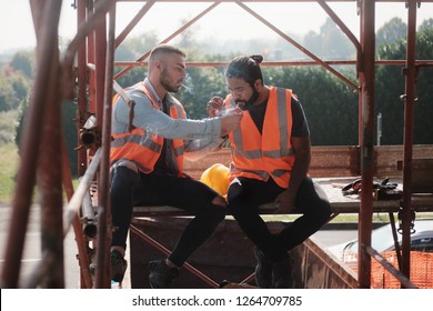 Two Happy Men Laughing At Work In Construction Site. Team Of Workers Smoking Cigarette And Talking During Break