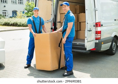 Two Happy Movers In Blue Uniform Loading Boxes In Truck