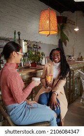 Two Happy Multicultural Female College Girls Sit In The Cafeteria, Chatting And Gossiping. Female Students And Girls Talk.