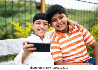 Two happy multiethnic kids taking selfie on mobile phone at park - concpet of friendship, religious diversity and social Harmony - Powered by Shutterstock