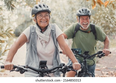 Two happy old mature people enjoying and riding bikes together to be fit and healthy outdoors. Active seniors having fun training in nature. - Shutterstock ID 2164850313