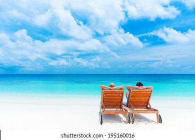 Two happy people relaxing on the beach, sitting down on comfortable sunbed and taking sunbath, rear view, summer holidays concept   
