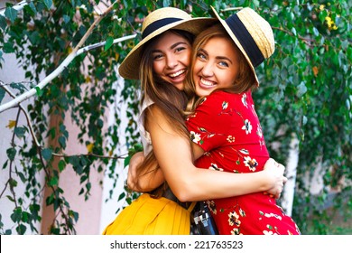 Two happy pretty young sisters, hugs smiling laughing  and having funny crazy time together, bearing stylish retro vintage feminine clothes and hats. Outdoors.