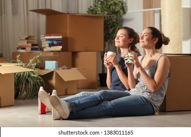 Two happy roommates moving home resting breathing fresh air sitting on the floor in the night