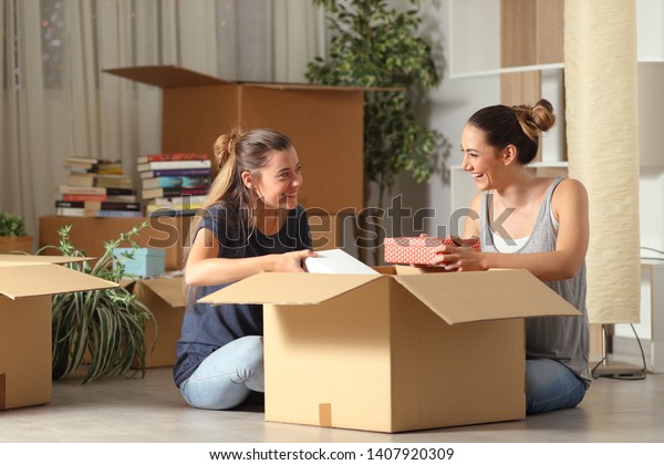 Two happy roommates talking unboxing gelongings\
moving home sitting on the\
floor