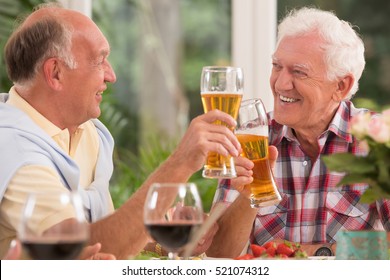 Two happy senior friends drinking a beer during dinner - Powered by Shutterstock