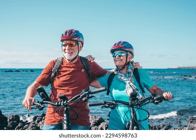 Two happy senior people enjoying riding bikes together at sea to be fit and healthy. Active senior couple wearing helmets having fun training in outdoors. Authentic elderly retired life concept - Powered by Shutterstock