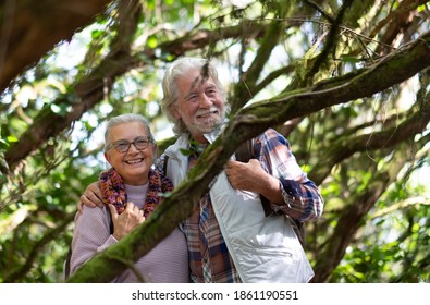 Two Happy Senior People Smiling Enjoying Mountain Hike In The Woods Among Trunks And Branches Covered With Moss During Autumn Season - Concept Of Fun And Active Retired Seniors