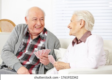 Two Happy Seniors Laughing Playing Cards Together In The Living Room